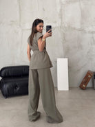 Frau in eleganter, olivgrüner Anzughose und Bluse posiert vor modernem Sofa. Mode, Damenbekleidung, stilvoll, zeitgemäßes Design.