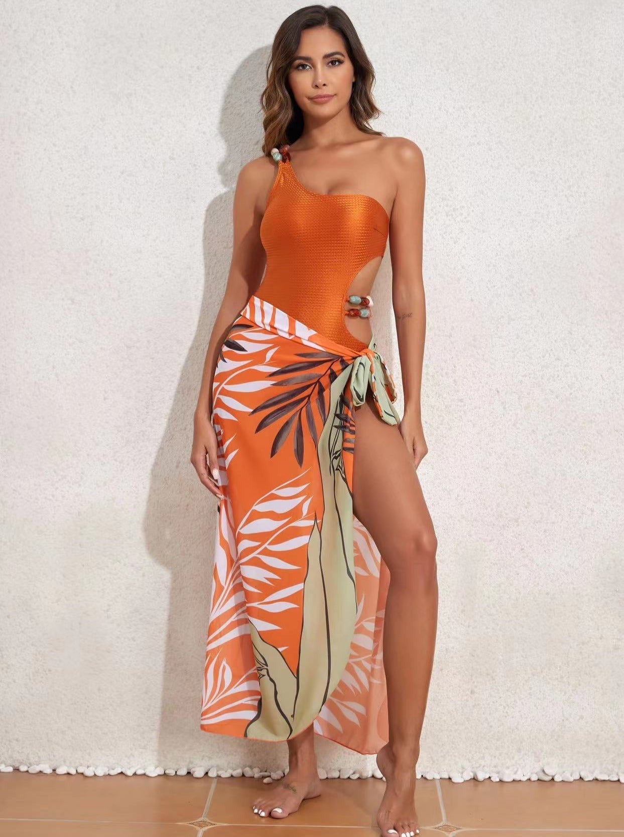 Frau in orangefarbenem Badeanzug mit tropischem Pareo, Strandmode, Sommeroutfit, elegantes Design, modische Bademode, Urlaubslook.