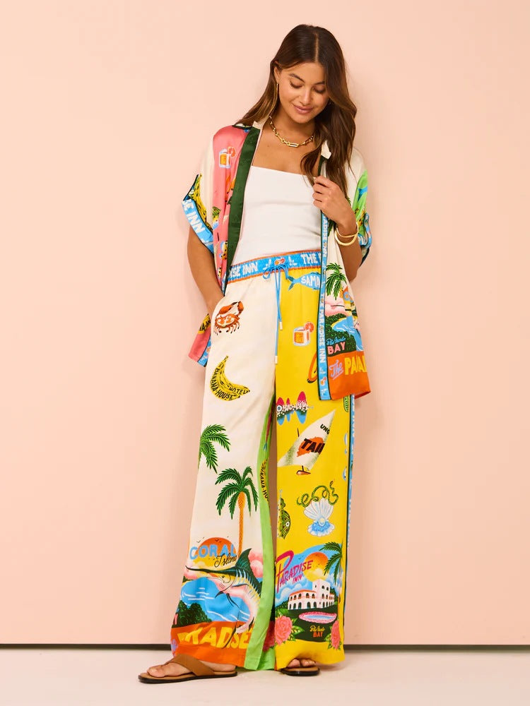 Frau in bunter Sommerkleidung mit tropischen Motiven, bestehend aus Hemd und Hose. Perfekt für Strandmode, Urlaub, tropische Outfits.