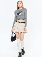 Junge Frau in grauem Pullover mit Hasenmotiv, beiger Faltenrock, Kniestrümpfe und schwarzen Schuhen. Modetrends, Streetwear, Damenmode.