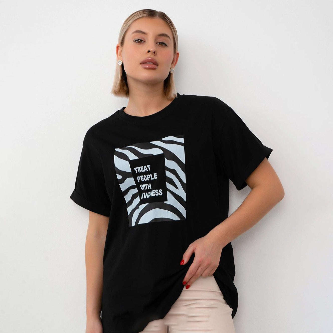 Frau trägt schwarzes T-Shirt mit "Treat People With Kindness"-Aufdruck, modisches Design, lässiger Stil, ideal für trendige Streetwear-Looks.