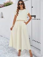 Elegantes Damen-Sommerkleid in Cremeweiß, fließend und ärmellos, ideal für Strandmode. Perfekt kombiniert mit Sandalen und Sonnenbrille.
