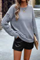 Damenpullover in Grau mit Zopfmuster-Ärmeln, kombiniert mit schwarzen Ledershorts. Modischer Herbstlook, ideal für kühle Tage.
