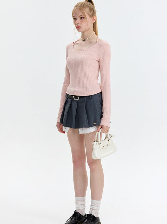 Junge Frau in rosa Pullover und grauem Faltenrock, hält weiße Handtasche. Modetrend, Damenmode, stilvolles Outfit, Freizeitlook.