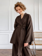 Frau in braunem Kimono-Set, lächelnd, vor weißer Wand. Modetrend, Damenbekleidung, eleganter Look, bequeme Mode, stilvolle Outfits.