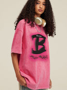 Frau trägt ein pinkes Oversize-T-Shirt mit großem "B"-Print und Kopfhörern um den Hals. Modetrend, Streetwear, lässiger Stil.