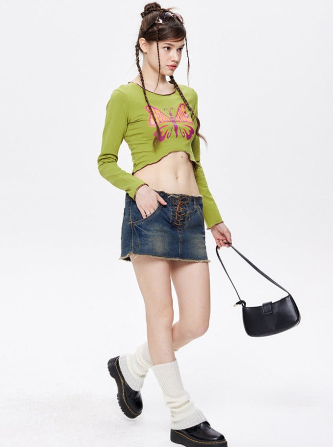 Junge Frau in grünem Crop-Top mit Schmetterlingsmotiv, Jeansrock, schwarzen Stiefeln und Handtasche. Modetrends, Streetwear, Damenmode.