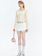 Frau in modischem Outfit: cremefarbener Pullover, weißer Rock, gepunktete Strumpfhose, silberne Schuhe, rosa Tasche. Trendige Damenmode 2023.