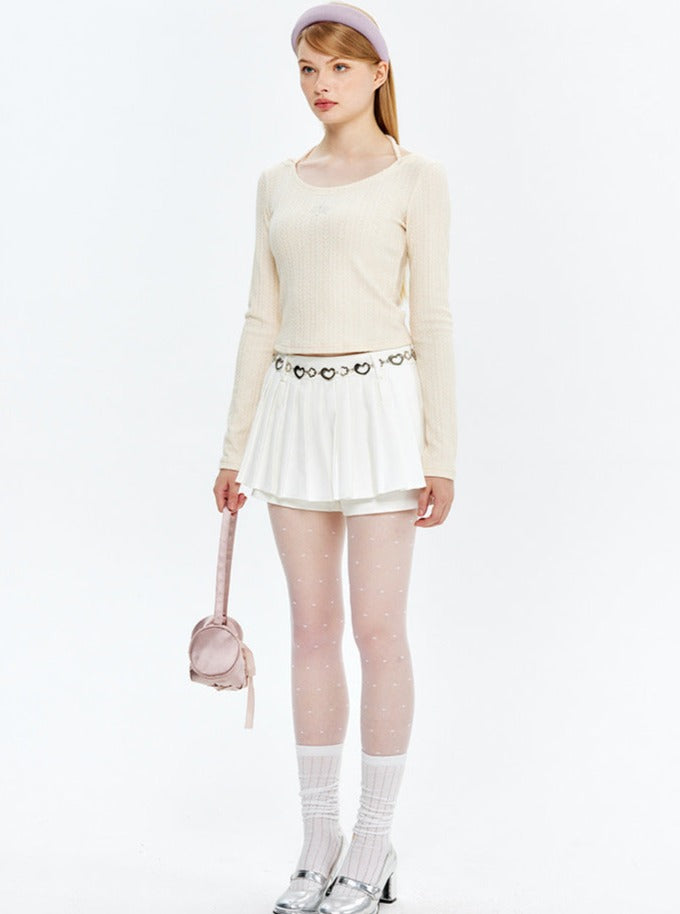 Frau in modischem Outfit: cremefarbener Pullover, weißer Rock, gepunktete Strumpfhose, silberne Schuhe, rosa Tasche. Trendige Damenmode 2023.