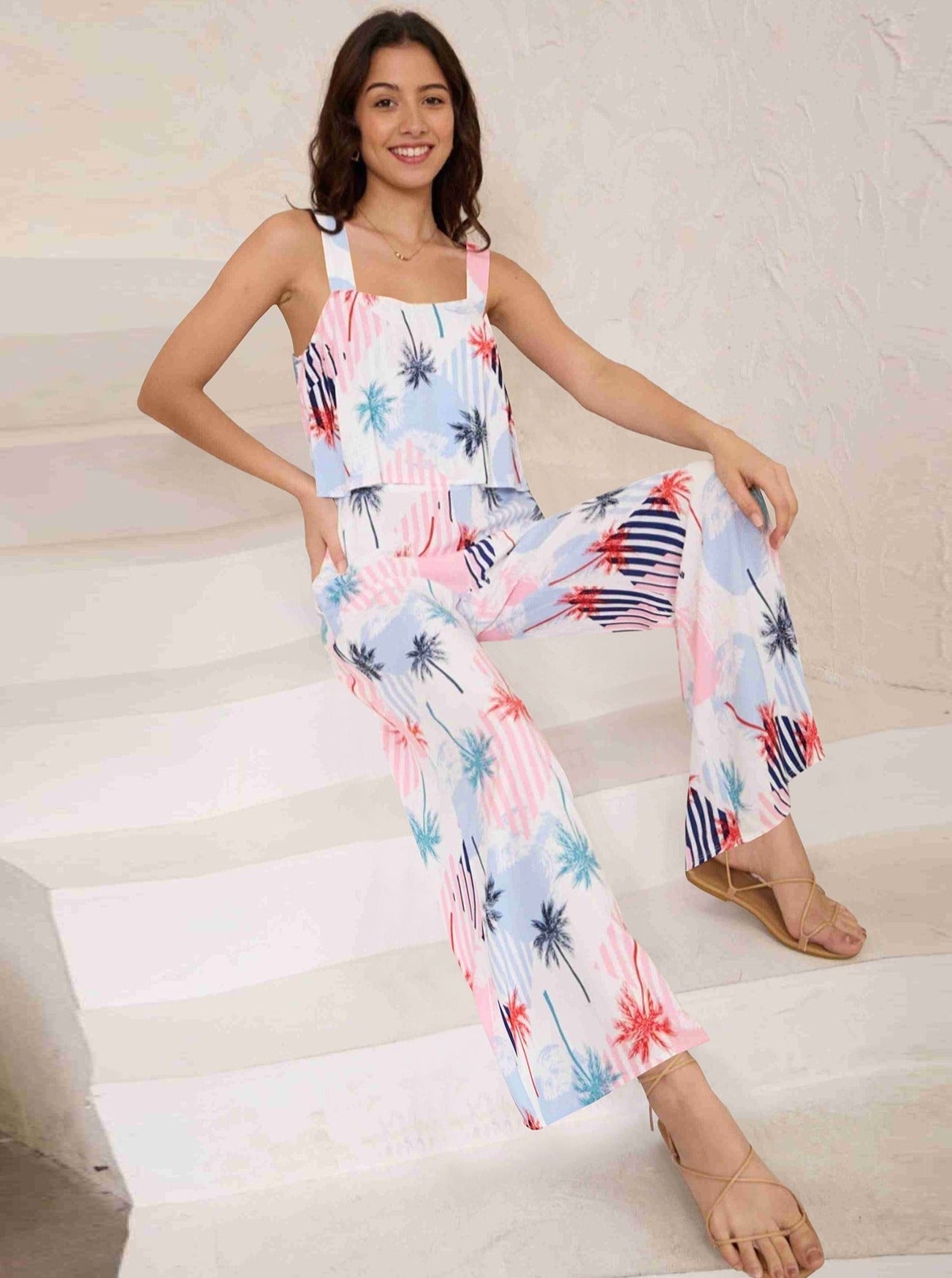 Frau in sommerlichem Jumpsuit mit Palmenmuster, sitzt auf Treppe. Modetrend, Damenmode, lässiger Stil, bequeme Kleidung, Sommeroutfit.