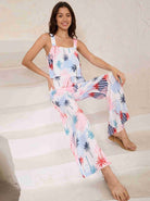 Frau in sommerlichem Jumpsuit mit Palmenmuster, sitzt auf Treppe. Modetrend, Damenmode, lässiger Stil, bequeme Kleidung, Sommeroutfit.