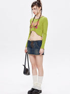 Junge Frau in grünem Crop-Top und Jeansrock, trägt schwarze Tasche und Stiefel. Modetrend, Streetwear, lässiger Stil, urbaner Look.