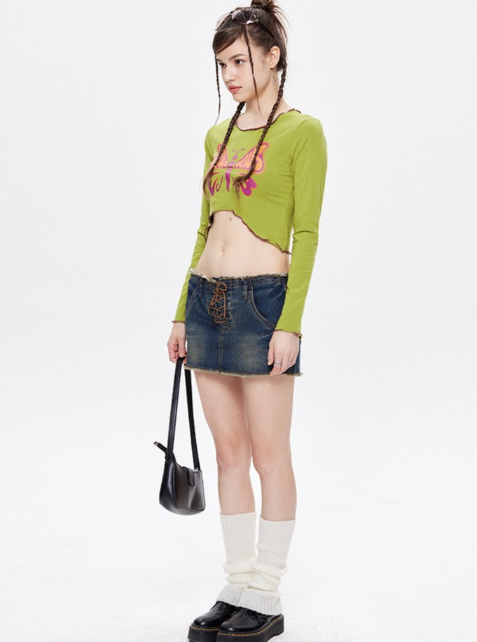 Junge Frau in grünem Crop-Top und Jeansrock, trägt schwarze Tasche und Stiefel. Modetrend, Streetwear, lässiger Stil, urbaner Look.
