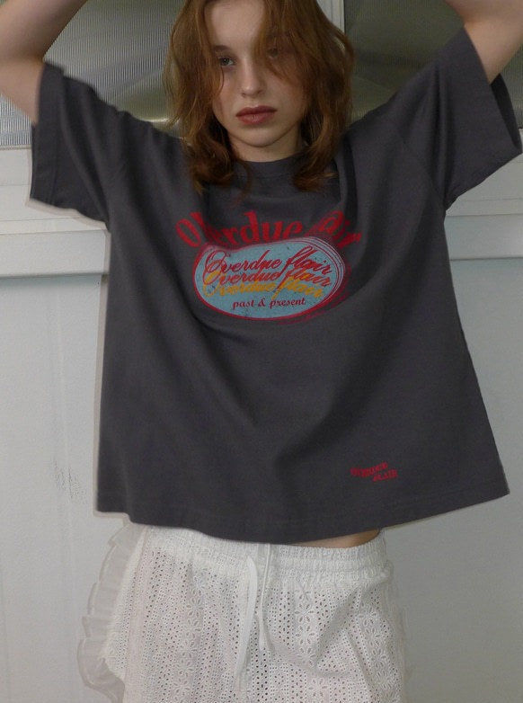Graues T-Shirt mit rotem Aufdruck "Overdue" und weißer Spitzenhose. Modetrend, lässiger Look, Streetwear, Damenmode, urbaner Stil.