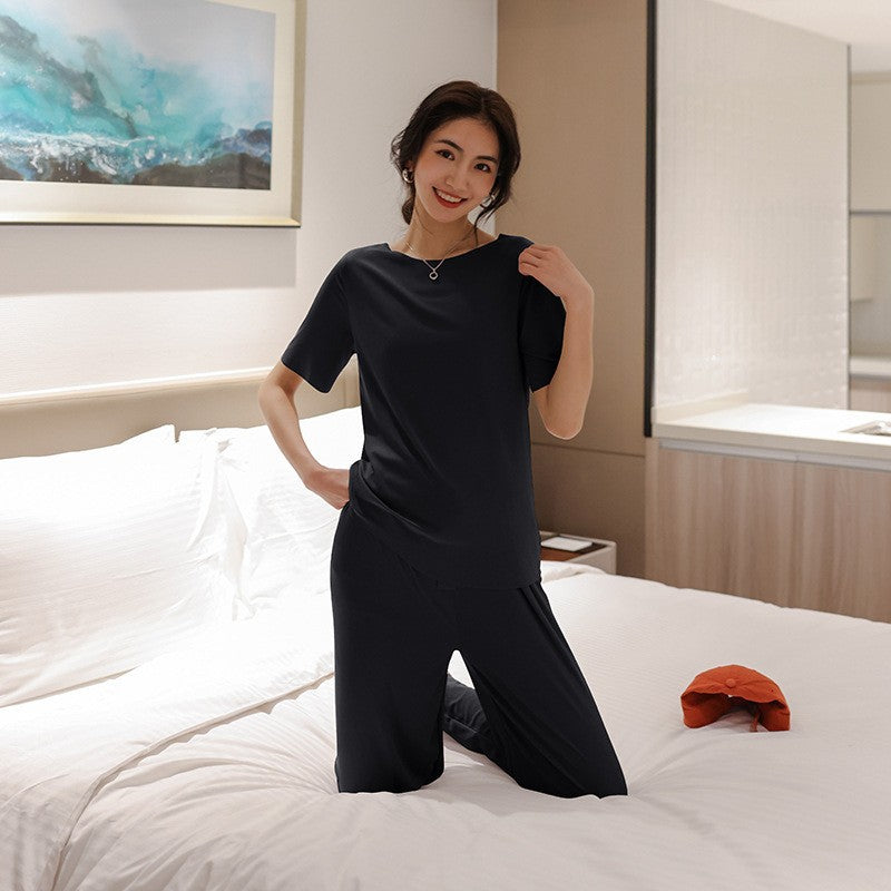 Frau in schwarzem Pyjama auf Bett, lächelnd. Bequeme Nachtwäsche, Schlafzimmer, entspannte Atmosphäre. Hochwertige Damenmode, Schlafanzug.