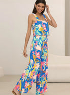 Frau in farbenfrohem, geblümtem Jumpsuit, ideal für Sommermode. Lebendige Blumenmuster, ärmelloses Design, modisch und bequem.