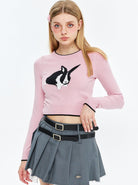 Junge Frau in rosa Pullover mit Kaninchenmotiv, grauem Faltenrock und schwarzem Gürtel. Modetrends, Damenbekleidung, Streetwear.