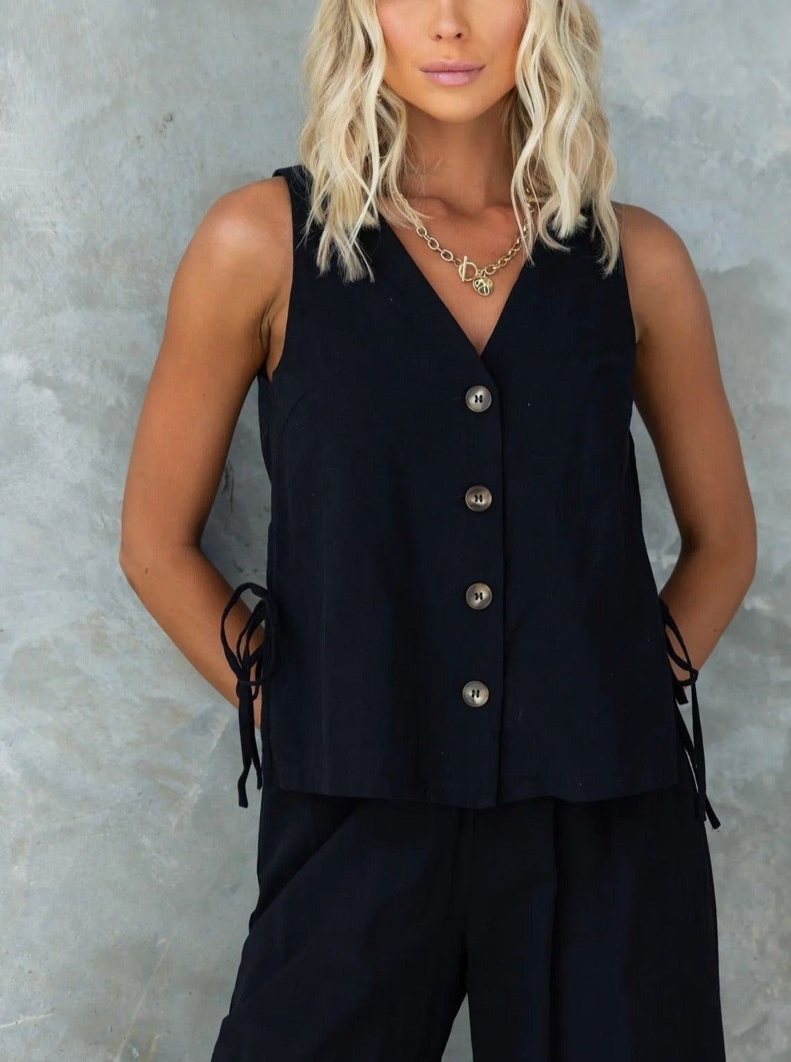 Ärmellose schwarze Weste mit Knopfleiste und seitlichen Schnürdetails, ideal für elegante Damenmode. Perfekt für stilvolle Outfits.