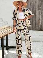 Frau in stilvollem, beigem Zweiteiler mit schwarzem Muster, Strohhut und Sandalen. Sommermode, lässiger Look, trendige Damenbekleidung.
