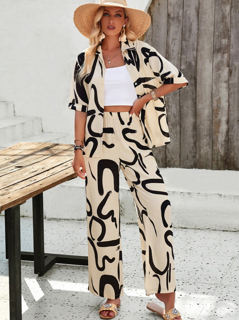 Frau in stilvollem, beigem Zweiteiler mit schwarzem Muster, Strohhut und Sandalen. Sommermode, lässiger Look, trendige Damenbekleidung.