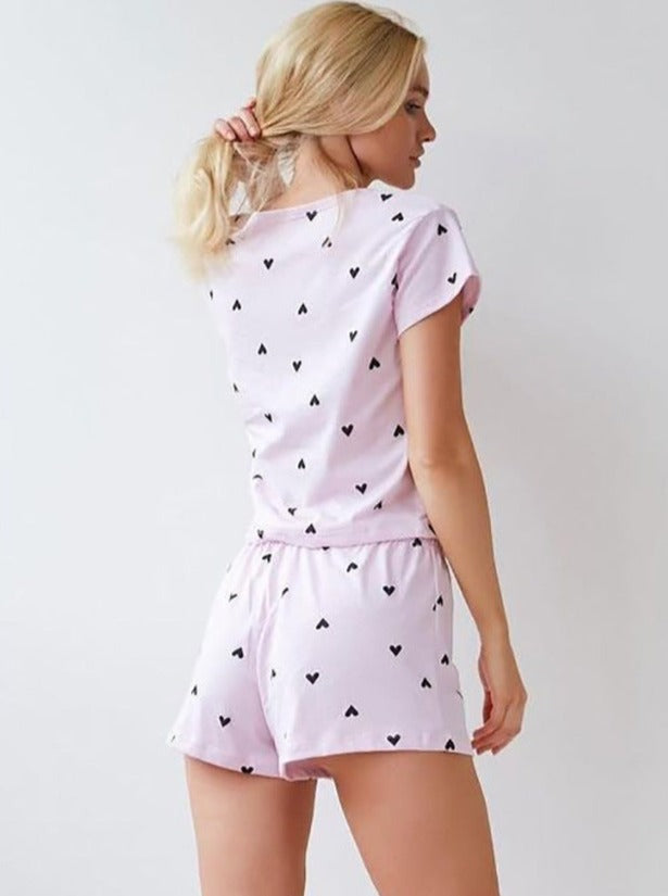 Frau in rosa Pyjama-Set mit Herzmuster, bequem und modisch, ideal für Damen-Nachtwäsche. Perfekt für entspannte Nächte und stilvolle Loungewear.