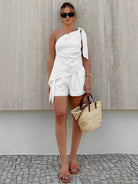 Frau in weißem, asymmetrischem Sommerkleid mit Strohtasche und Sandalen. Modetrend, Sommeroutfit, stilvolle Damenmode, lässiger Chic.