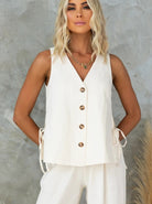 Ärmellose Damenbluse in Cremeweiß mit Knopfleiste, V-Ausschnitt und seitlichen Schleifen. Elegante Sommermode, ideal für stilvolle Outfits.