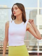 Frau in weißem Sporttop und gelber Leggings auf Tennisplatz. Fitnessmode, Sportbekleidung, athletischer Look, urbaner Hintergrund.