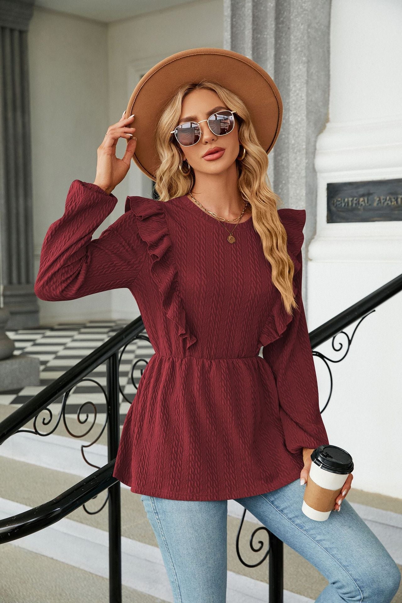 Frau in rotem Rüschenpullover, blauer Jeans und Hut hält Kaffeebecher. Modetrend, Herbstmode, stilvolle Damenbekleidung, Accessoires.