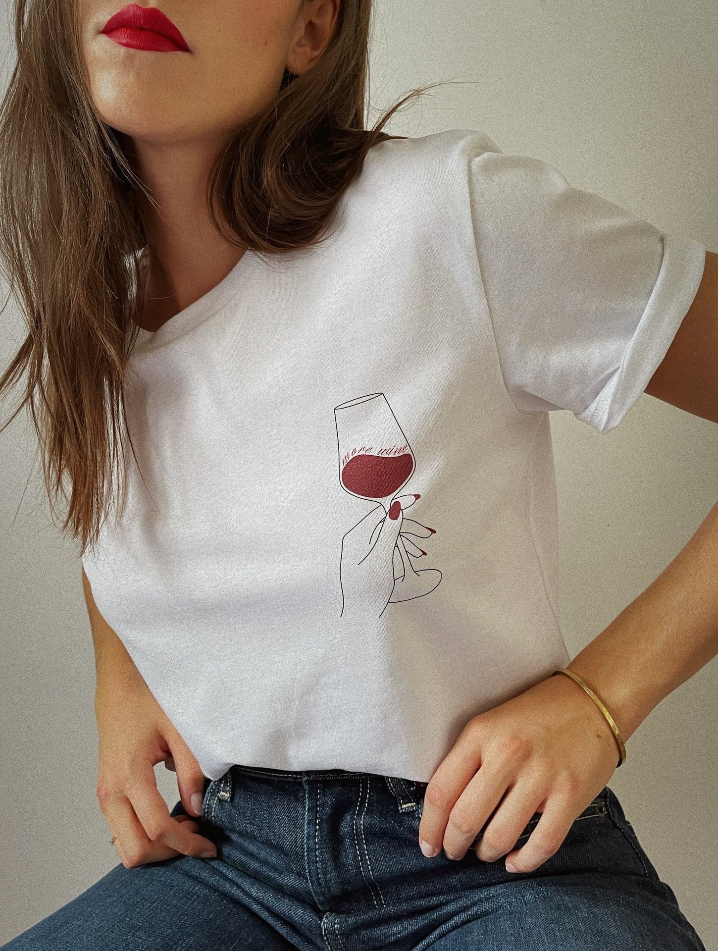 Frau trägt weißes T-Shirt mit stilisiertem Weinglas-Design, kombiniert mit blauer Jeans. Modetrend, minimalistisches Design, lässiger Look.