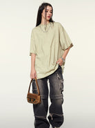 Frau in übergroßem T-Shirt und zerrissenen Jeans, hält eine braune Designer-Handtasche. Streetwear, modisch, lässiger Stil, Trend 2023.