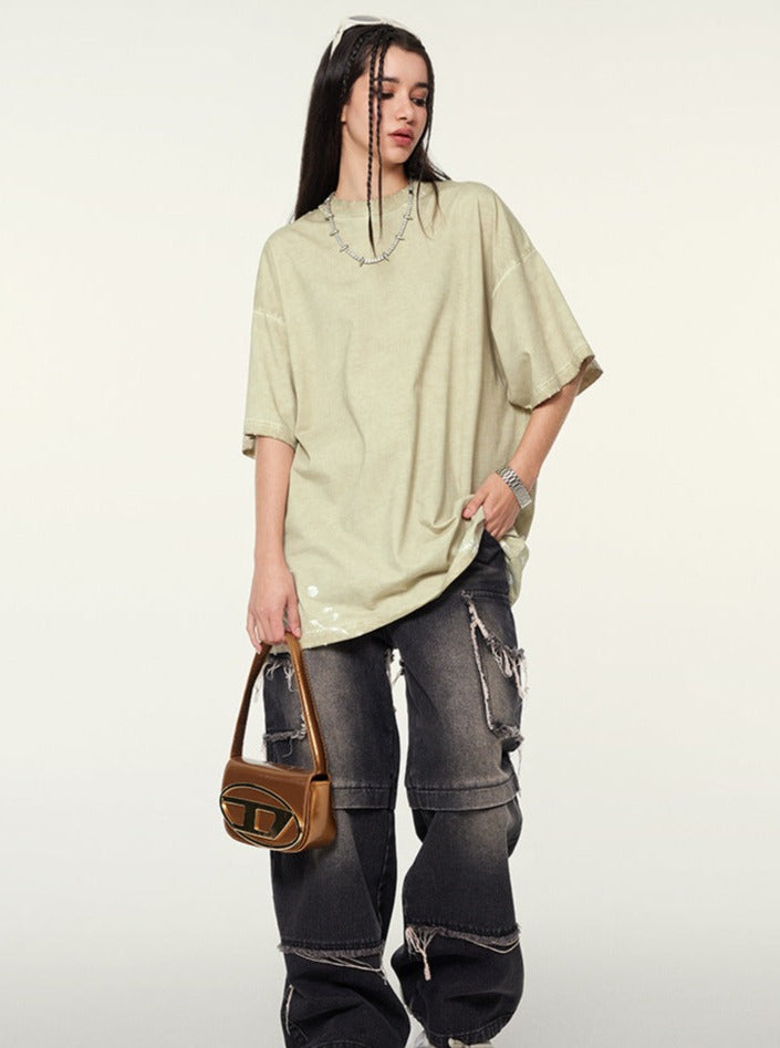 Frau in übergroßem T-Shirt und zerrissenen Jeans, hält eine braune Designer-Handtasche. Streetwear, modisch, lässiger Stil, Trend 2023.