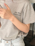 Graues T-Shirt mit Aufdruck "The Way - Determine", getragen von Person, kombiniert mit hellblauer Jeans. Modetrend, lässiger Stil, Streetwear.