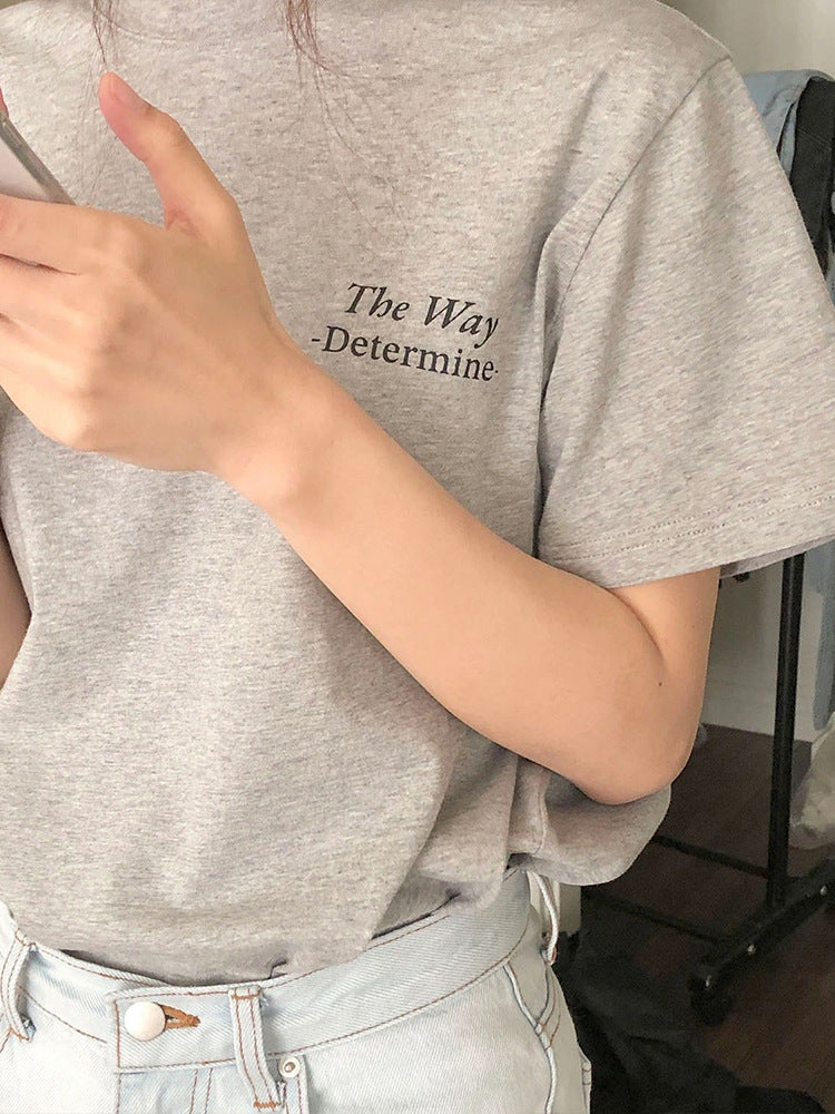 Graues T-Shirt mit Aufdruck "The Way - Determine", getragen von Person, kombiniert mit hellblauer Jeans. Modetrend, lässiger Stil, Streetwear.