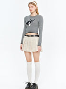 Junge Frau in grauem Pullover mit Tiermotiv, beiger Faltenrock, Kniestrümpfe und schwarzen Schuhen. Modetrends, Streetwear, Damenmode.