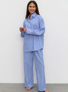 Frau in gestreiftem blauen Pyjama-Set, lächelnd, vor weißem Hintergrund. Bequem, modisch, Nachtwäsche, Damenmode, Schlafanzug.