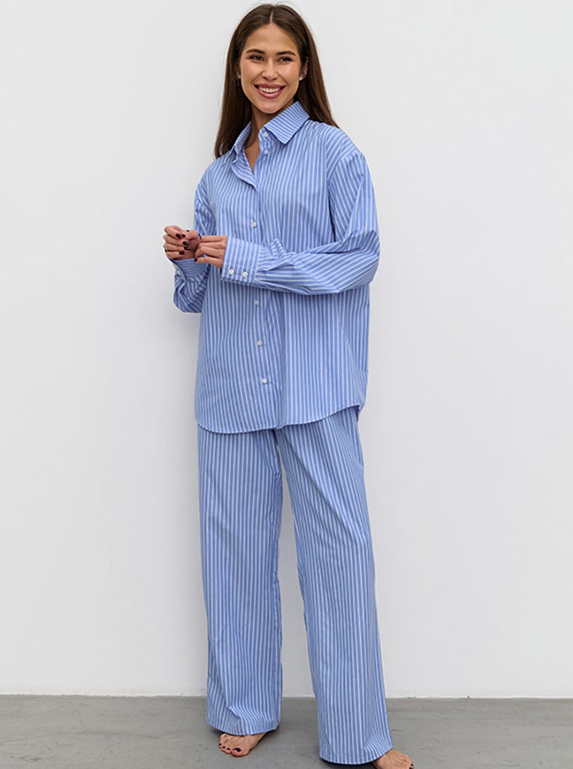 Frau in gestreiftem blauen Pyjama-Set, lächelnd, vor weißem Hintergrund. Bequem, modisch, Nachtwäsche, Damenmode, Schlafanzug.