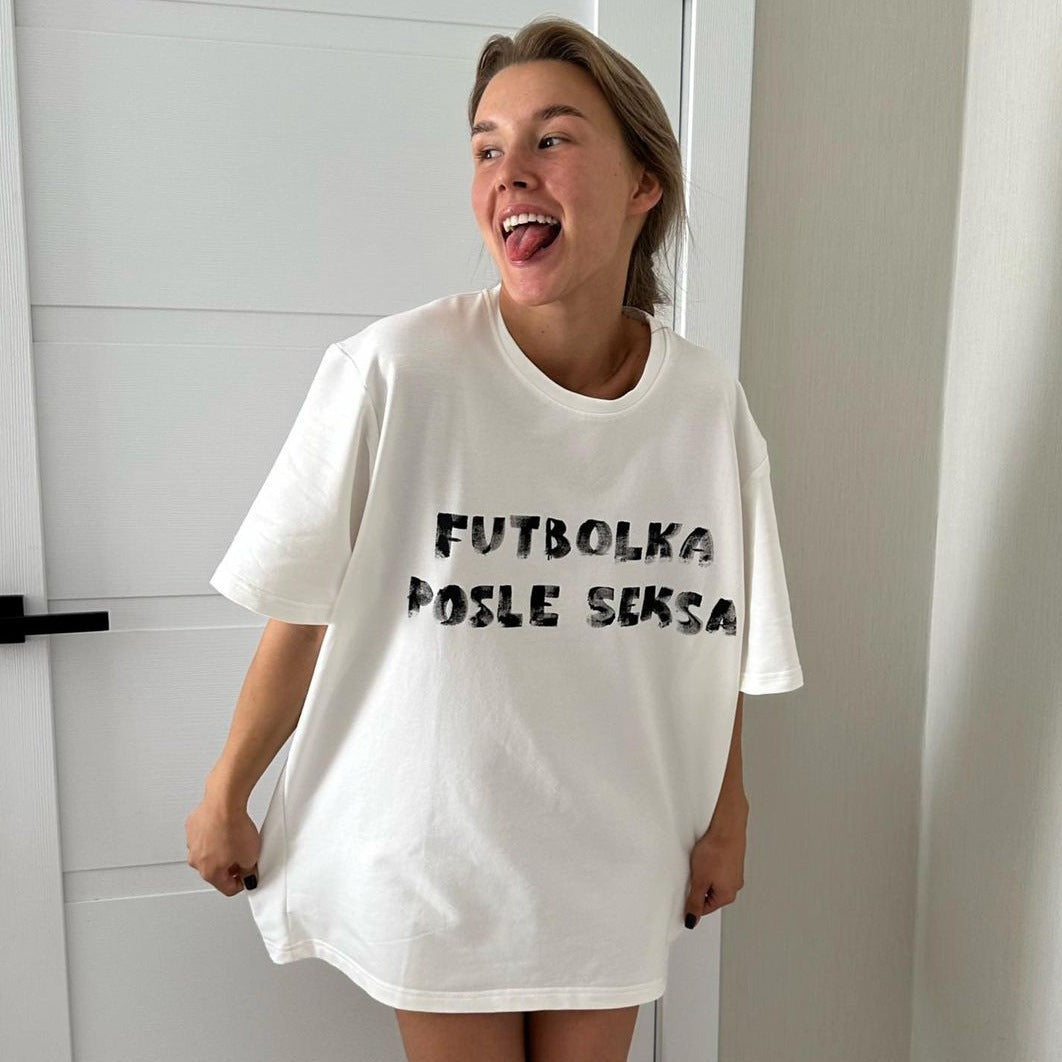 Frau trägt weißes T-Shirt mit Aufdruck "Futbolka Posle Seksa", lässiger Stil, modisches Design, trendige Damenbekleidung, bequemes Outfit.