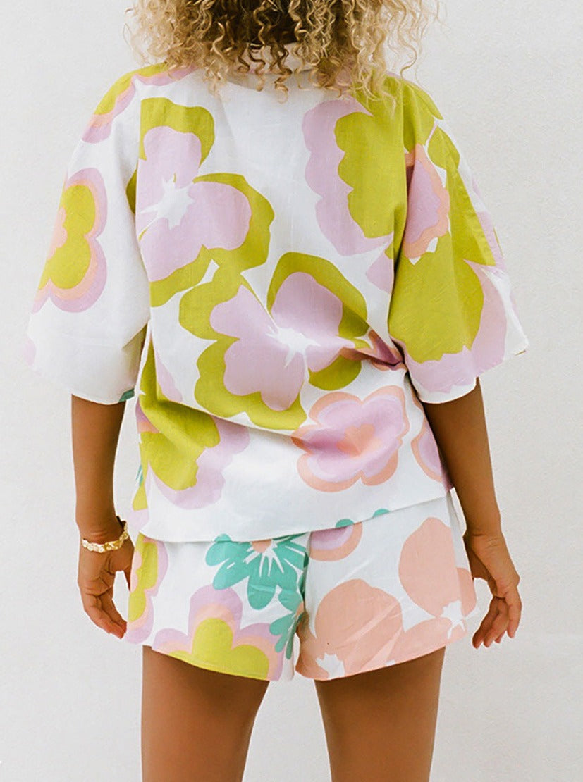 Frau in bunter Sommerkleidung mit floralen Mustern, bestehend aus kurzärmligem Oberteil und Shorts. Perfekt für Strandmode und Freizeitoutfits.
