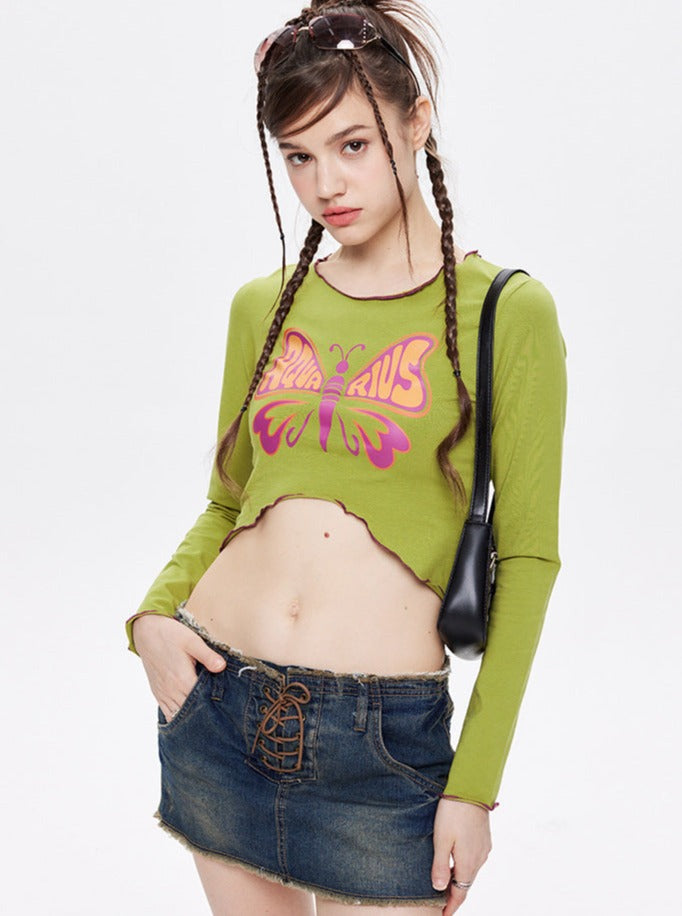 Junge Frau in grünem Langarmshirt mit Schmetterlingsmotiv und Jeansrock. Modetrend, Streetwear, lässiger Stil, jugendliche Mode, urbaner Look.