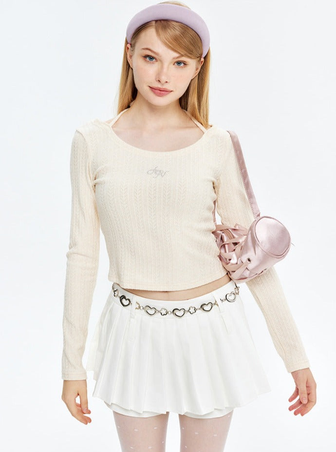 Junge Frau in modischem, cremefarbenem Langarmshirt und weißem Faltenrock, trägt rosa Stirnband und Tasche. Trendige Damenmode, stilvoll.