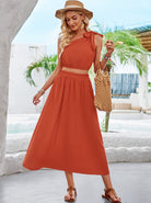 Elegantes Sommerkleid in Terrakotta, ärmellos mit Schleifendetail, kombiniert mit Strohhut und Sandalen. Perfekt für Strandmode und Urlaubsoutfits.