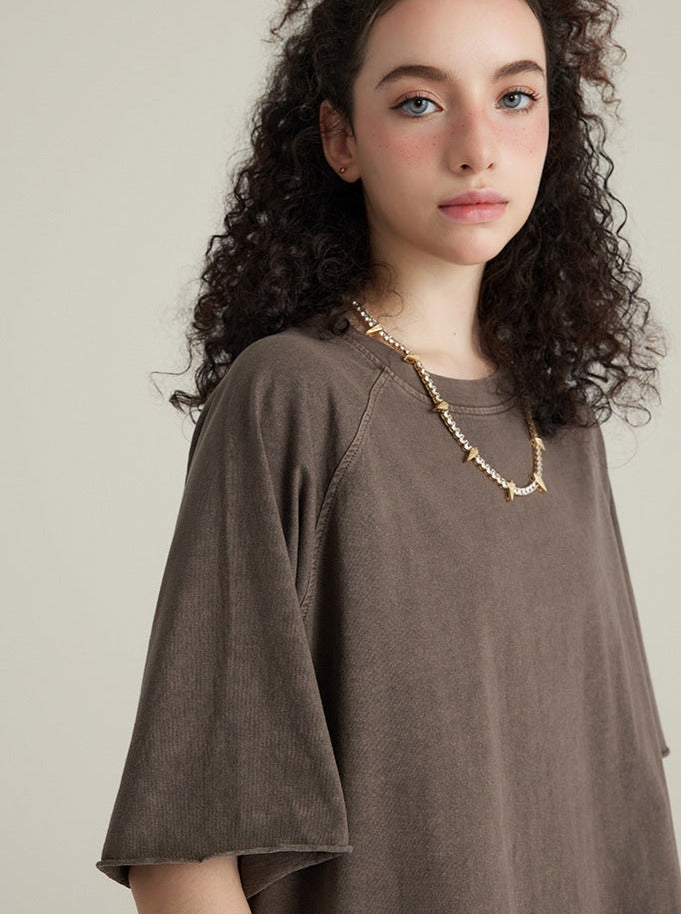 Frau in braunem T-Shirt mit lockigem Haar und Perlenkette. Mode, Damenbekleidung, lässiger Stil, Schmuck, trendige Outfits.