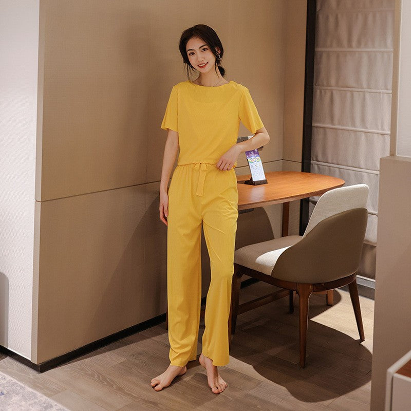 Frau in gelbem Pyjama steht barfuß im modernen Wohnzimmer. Bequeme Nachtwäsche, stilvolles Design, gemütliche Atmosphäre, entspannte Mode.