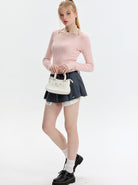 Junge Frau in rosa Pullover und grauem Rock, hält weiße Handtasche. Modetrend, Damenmode, stilvolle Kleidung, lässiger Look, Streetstyle.