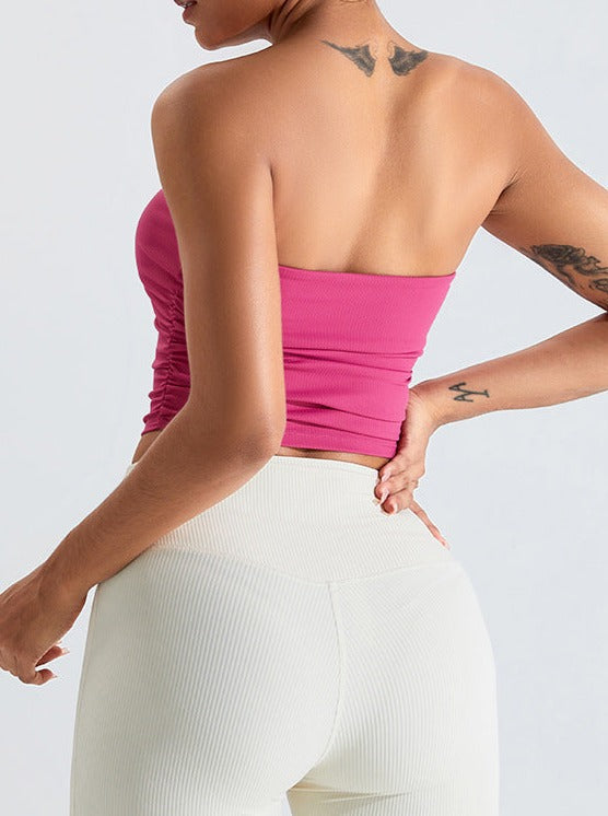 Frau in rosa trägerlosem Top und weißen Leggings, zeigt Rückenansicht. Modetrend, Sommeroutfit, sportlich-elegant, Freizeitkleidung.