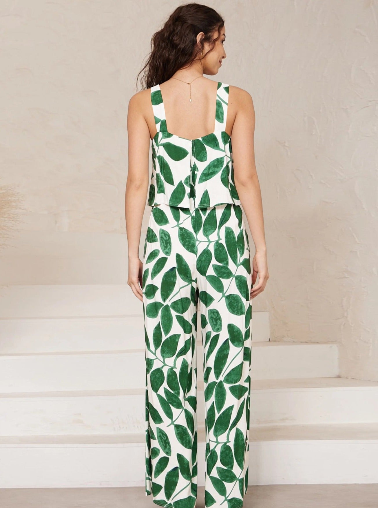 Frau in ärmellosem, grün-weißem Blattmuster-Jumpsuit, modisch, sommerlich, elegant, ideal für Freizeit und Strand, trendige Damenmode.
