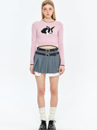 Junge Frau in rosa Pullover mit Hasenmotiv, grauem Faltenrock und schwarzen Schuhen. Modetrend, Streetwear, jugendlicher Stil, 2023.