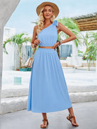 Elegantes Sommerkleid in Hellblau, ärmellos mit Schleifendetail, ideal für Strandmode. Perfekt kombiniert mit Strohhut und Sandalen.