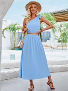 Elegantes, blaues Sommerkleid mit asymmetrischem Schnitt, ideal für Strandmode. Perfekt kombiniert mit Strohhut und Sandalen für einen stilvollen Look.